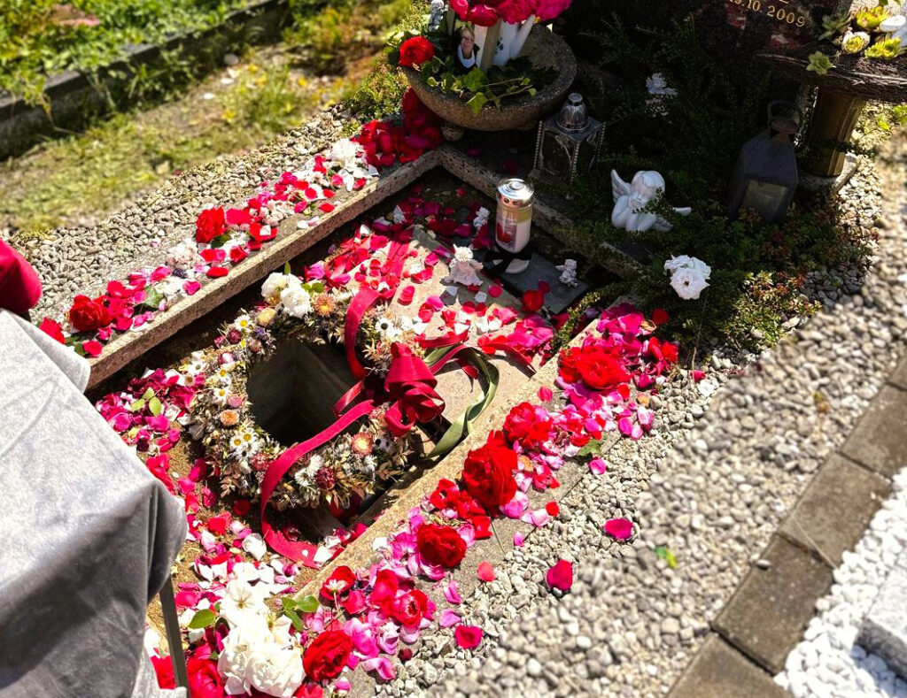 Leeres Grab vor Beisetzung einer Urne, mit Blumenblättern und Rosenblättern geschmückt